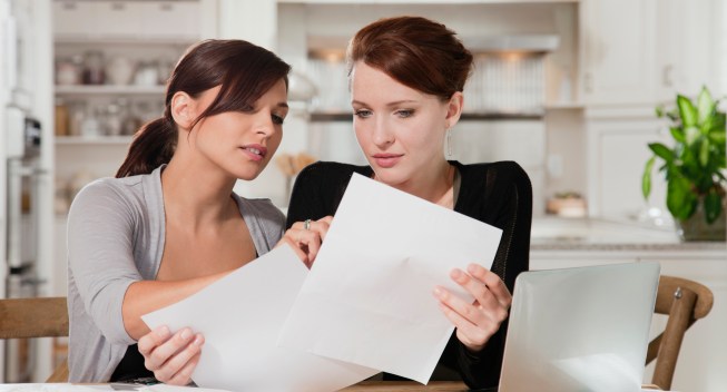 Two young women doing paperwork at kitchen table