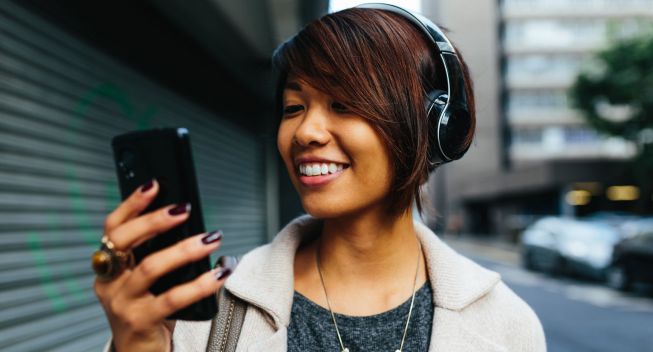 Young Businesswoman listening music on the Street with Headphones.