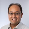 Pratik Wadher, SVP, Product Development smiling at the camera wearing a tan shirt and glasses.