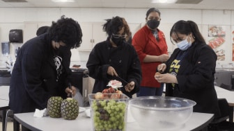 High school students wearing masks cut fruit during culinary arts class.