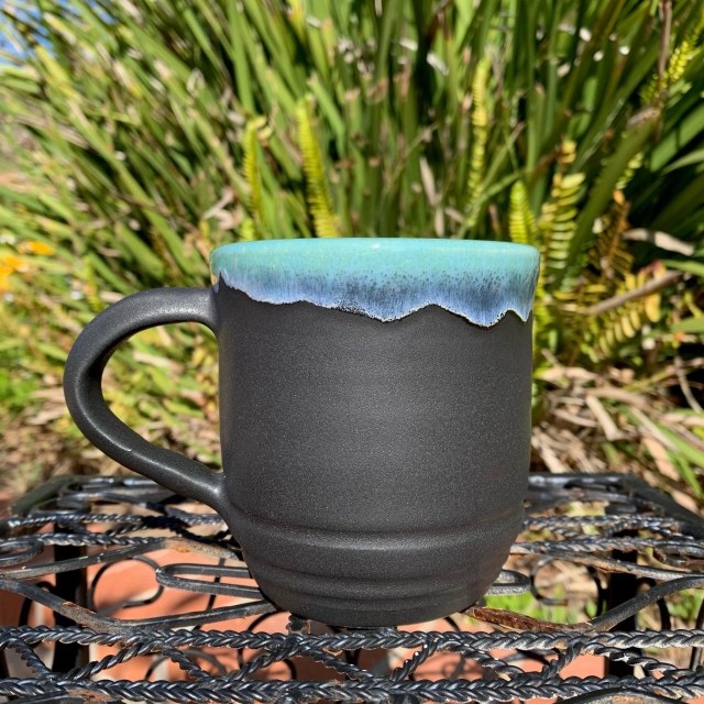 A black mug with a glossy, sky blue rim.