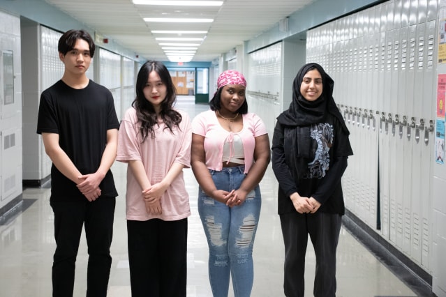Four high schoolers pose in a locker-lined hallway.