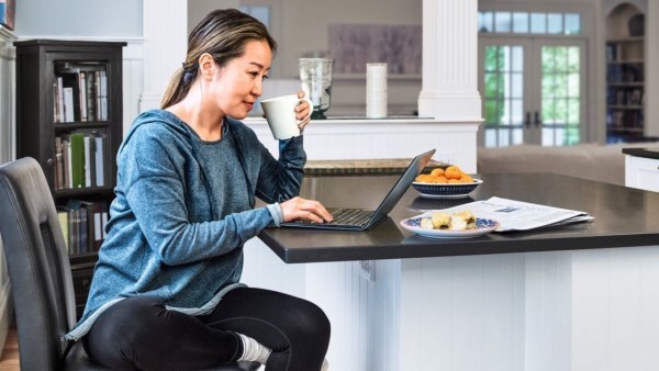 A woman sits at her kitchen counter while scrolling at her computer.