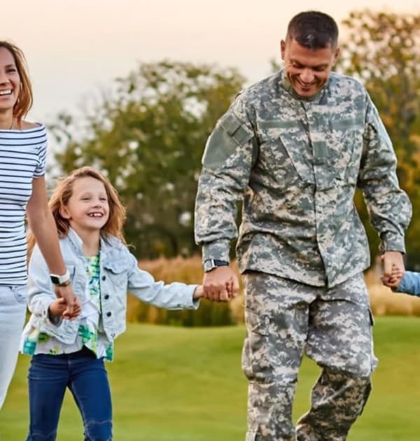 A husband in his military uniform is walking outside with this wife and two young daughters.