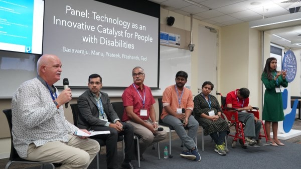 A diverse group of people on stage with a background reading, "Technology as an innovative catalyst for people with disabilities.: