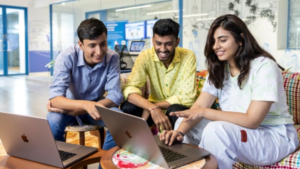A group of Indian technology professionals collaborate around a laptop in a corporate office.