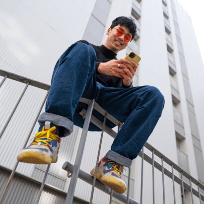 A young man sits on a fence in a city, looking at his phone.