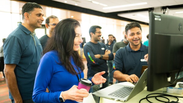 Various happy individuals gathered around a computer screen.