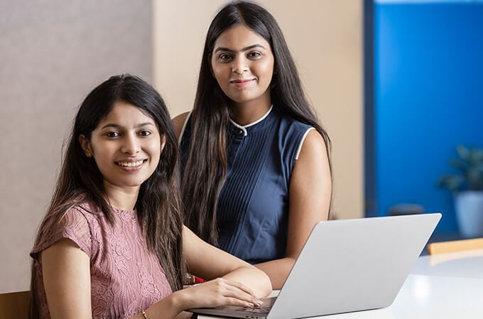 Two people are smiling and sitting at a laptop.
