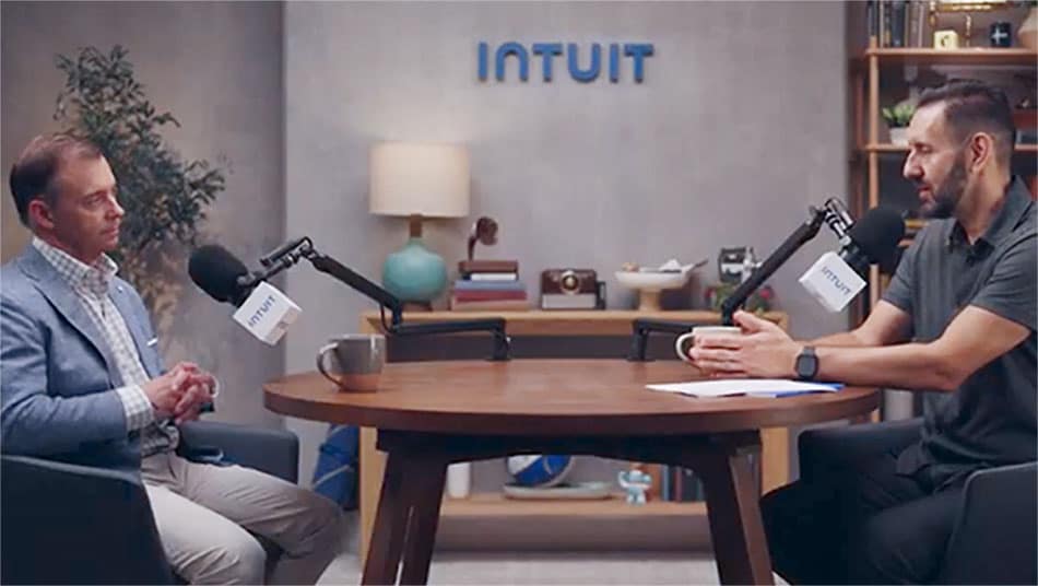 A person and person sitting at a table with a laptop.