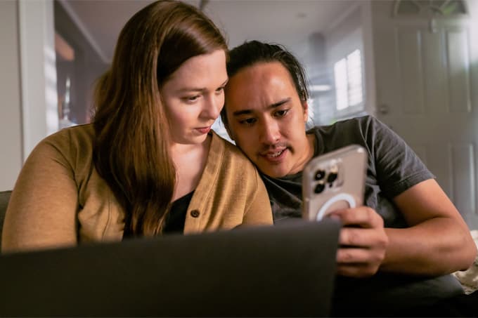 Couple looking at a phone in front of laptop