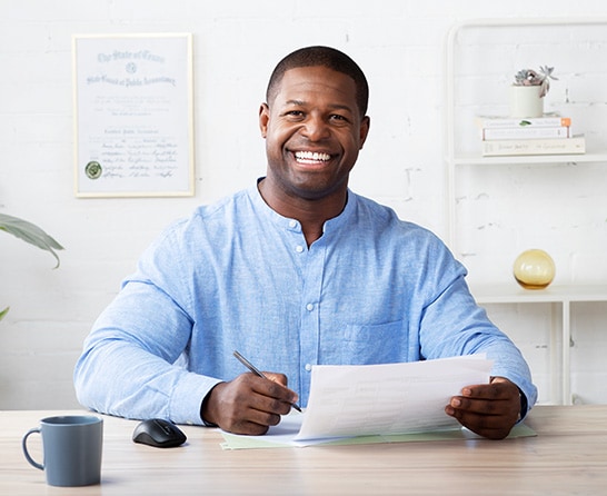 An Intuit Expert, sitting on his desk with papers and a coffee mug, smiling. 