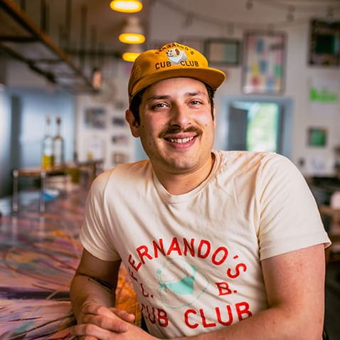 A person wearing a yellow cap and t-shirt with hands folding and smiling