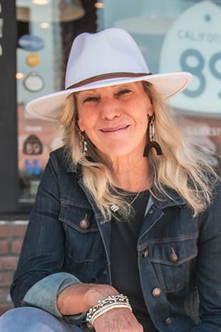 A woman wearing jean jocket, hat, and smiling