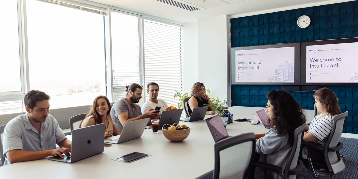 A group of people sitting around a table with laptops.