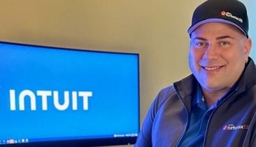 A person in a hat is standing in front of a computer.