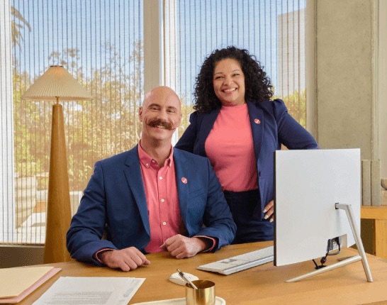 A person and person sitting at a desk with a laptop.