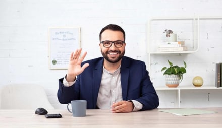 A person in a blue shirt and a tie smiles while holding a glass.