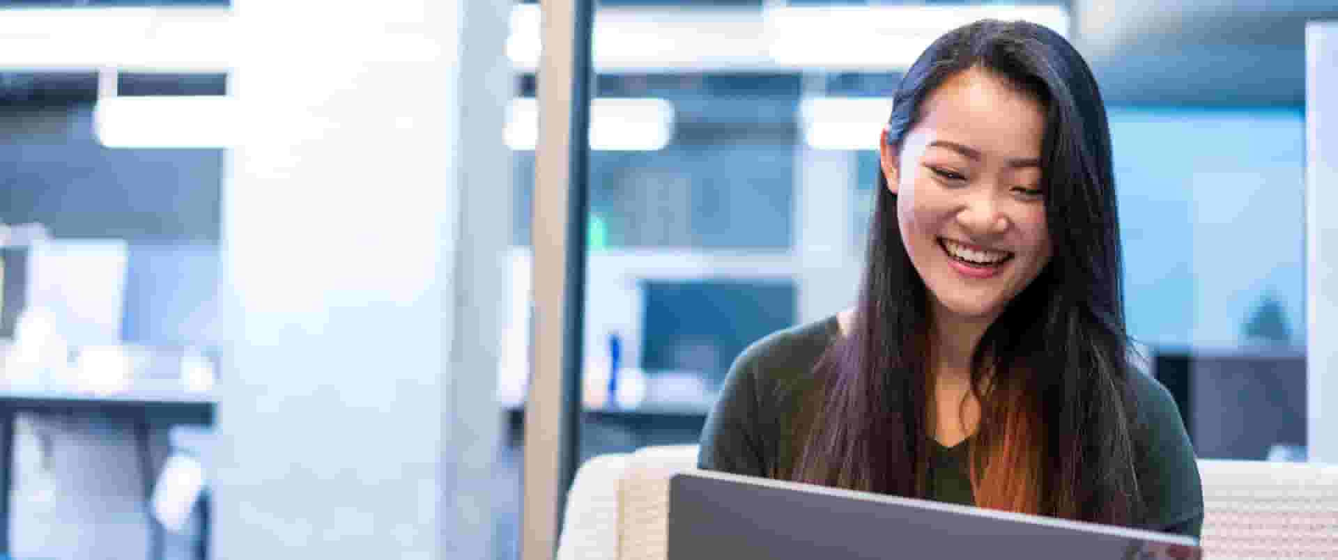 female-employee-early-career-photo-icom-desktop-1920x804.jpeg A person smiling while looking at a laptop.
