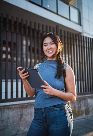 A person holding a tablet standing next to a building.
