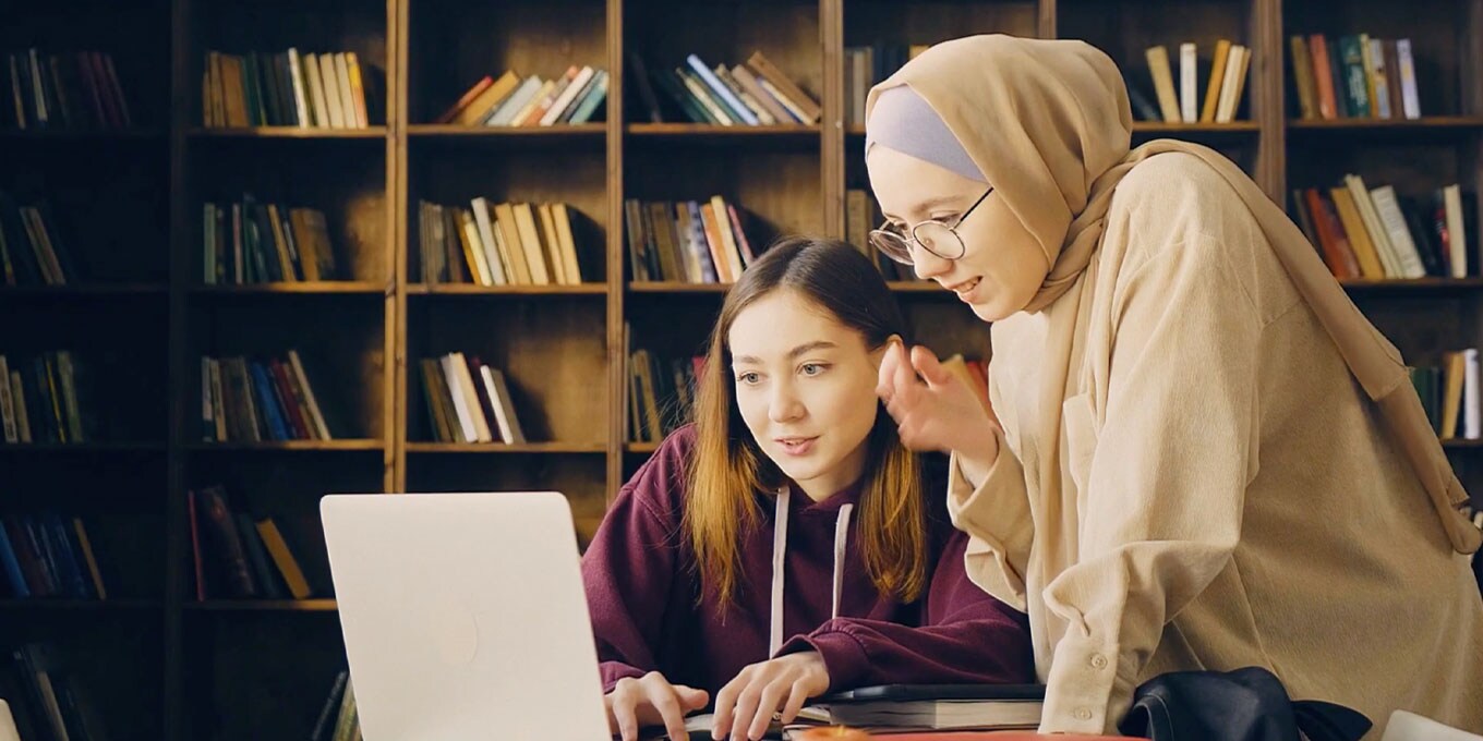 Two female students using at laptop in a library