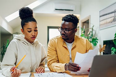 Two people sitting at a desk looking at a laptop.