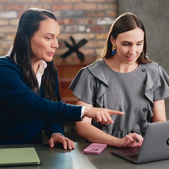 Two people sitting at a table talking and looking at a laptop
