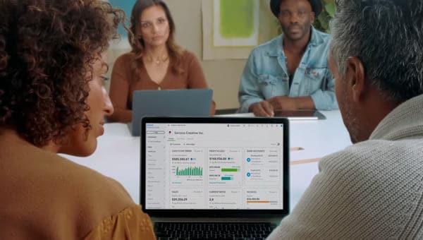 A group of people sitting around a laptop computer.