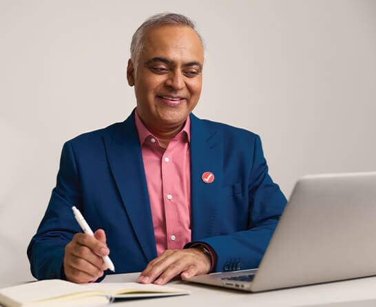 A person in a pink shirt and a pink tie is looking at a laptop.