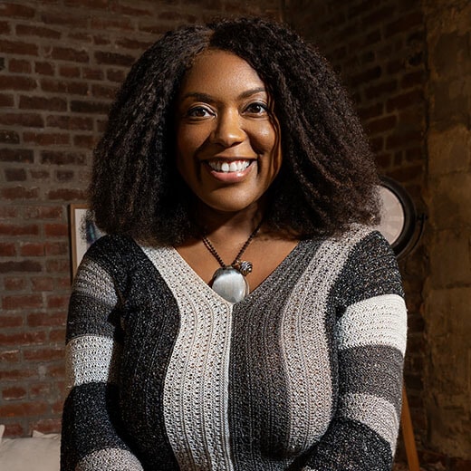 IDEAS participant Shannon Bobo, sitting on a chair smiling and holding a cup.