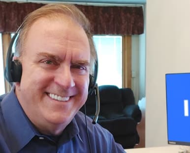 A person smiling and holding a cell phone to his ear.