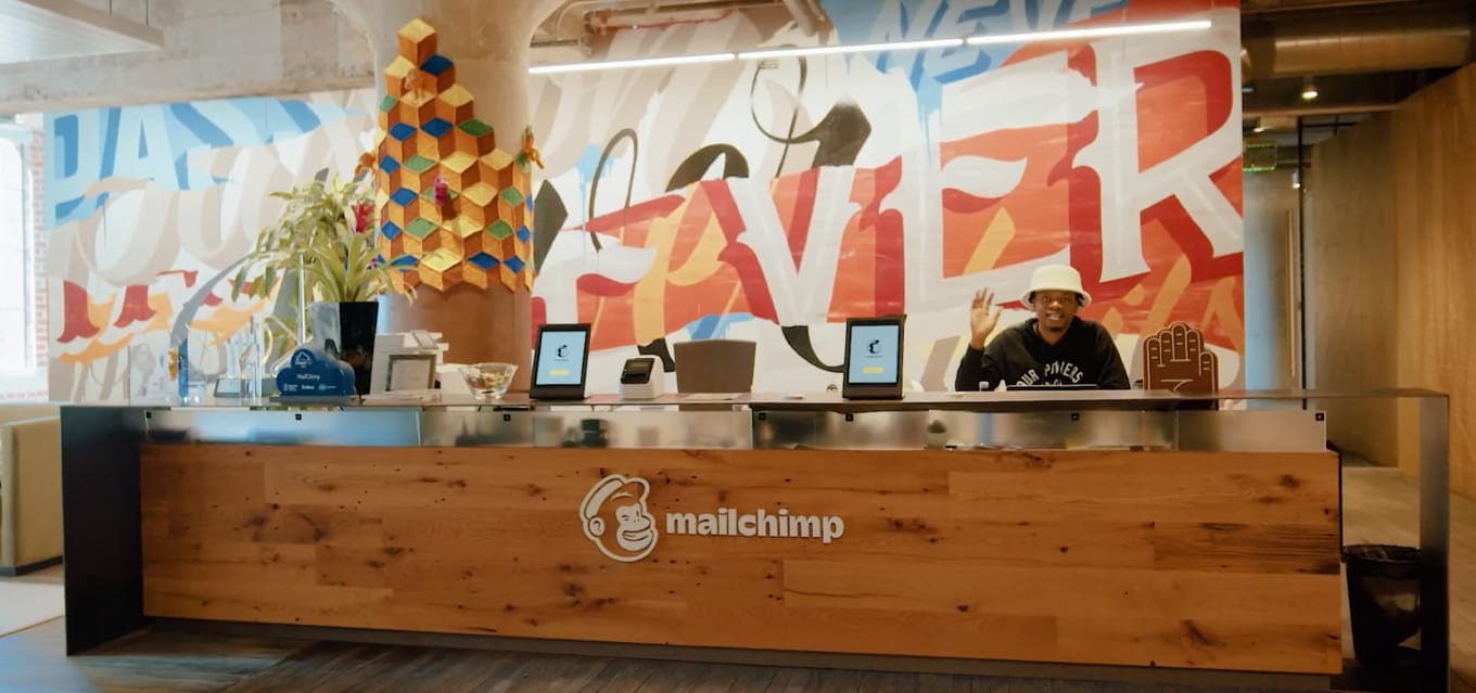 Mailchimp employee waiving behind a desk.