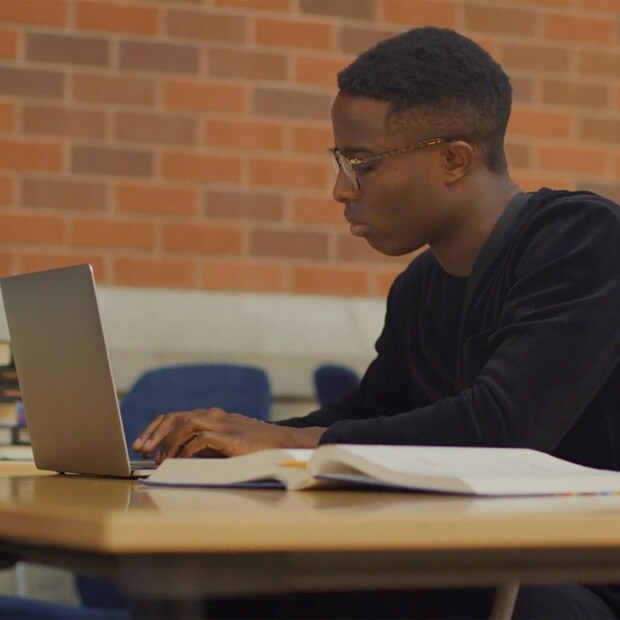 Male student studying on a desk with his laptop and book