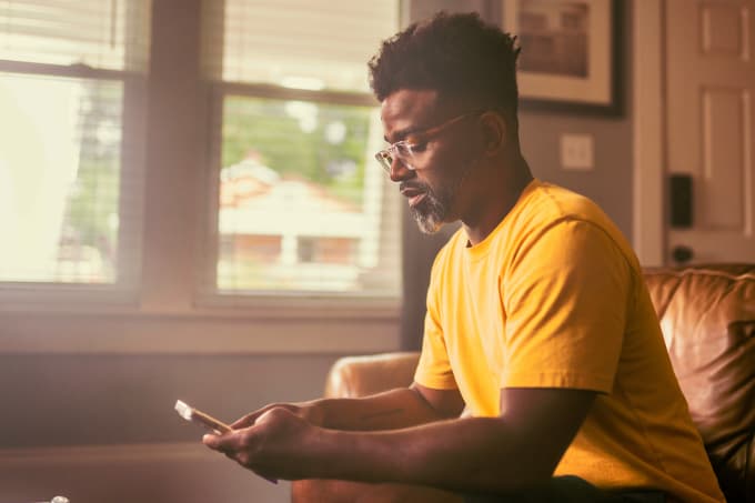man-checking-phone-photo-icom-desktop-680x453.jpeg Man sitting on a couch checking his phone