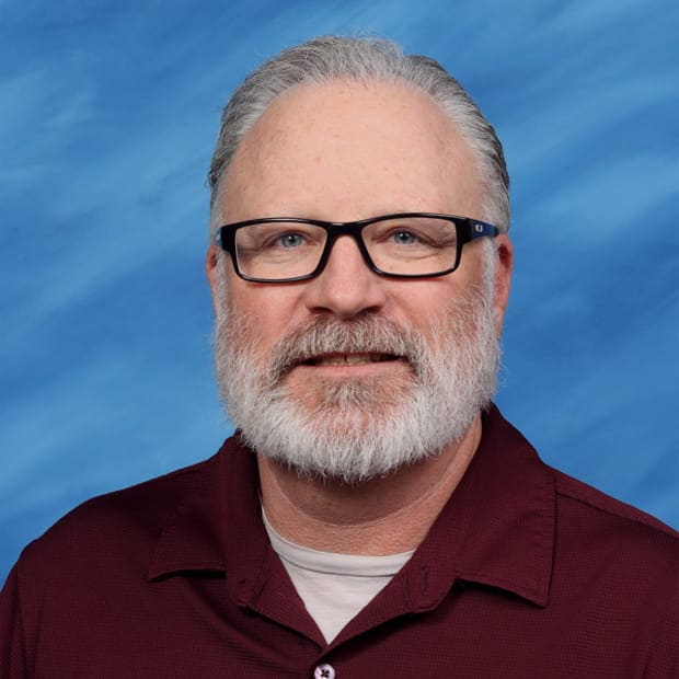 A person with glasses and a tie smiles.