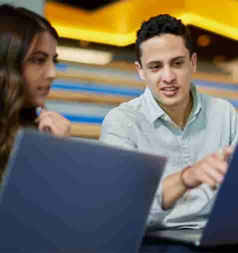 A person and person sitting at a table with laptops.