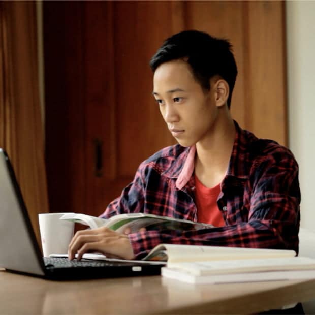 Student using a laptop to study while holding a book