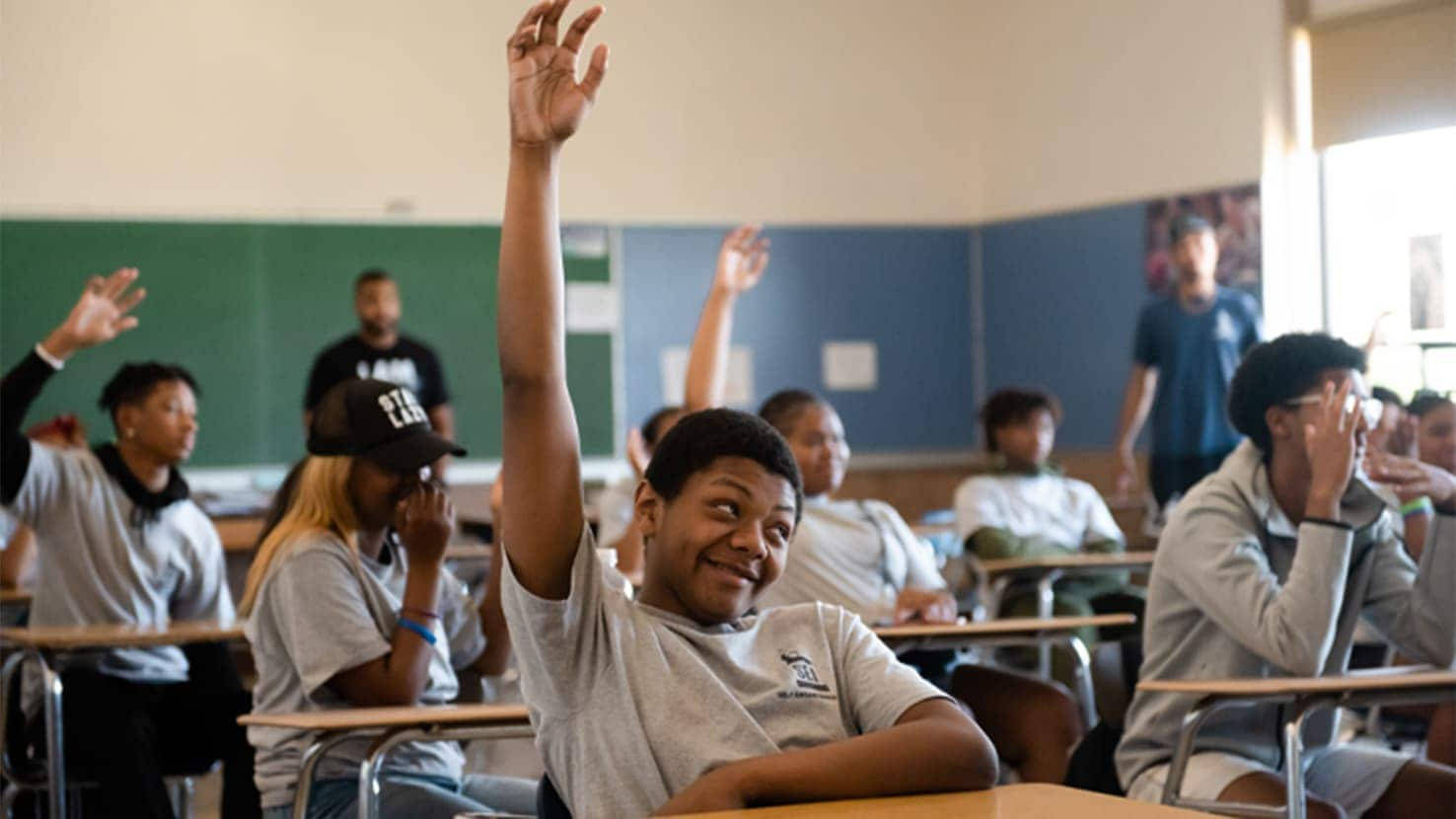 Group of students raising their hands in a classroom.