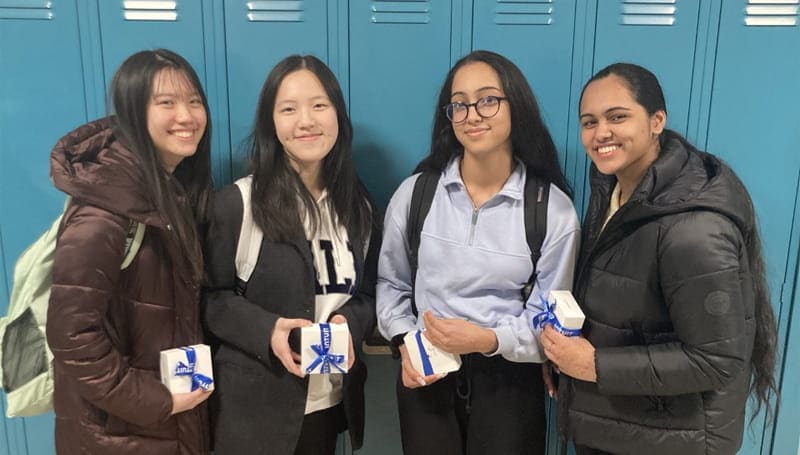 Four students in a hallway holding gift boxes.