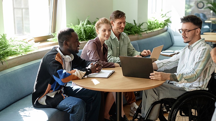 A group of people sitting around a table with laptops talking about Intuit Enterprise Suite Spring update features